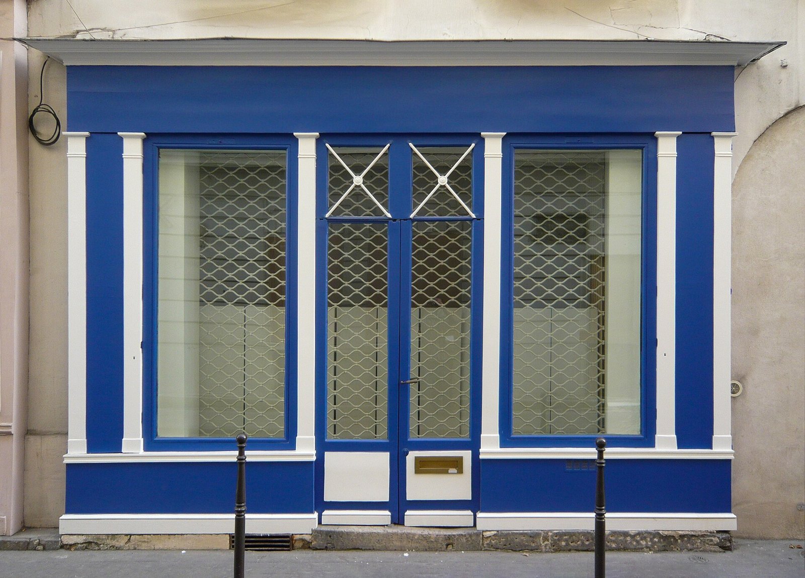 Vitrine réelle de boutique parisienne avec grilles de protection visibles derrière les vitrages